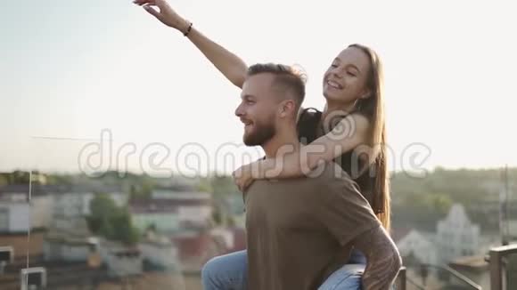爱你一个女孩站在一个男人的肩膀上她的手举起来在屋顶上带着表情微笑视频的预览图