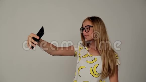 美丽的金发女郎戴着眼镜在智能手机上自拍视频的预览图