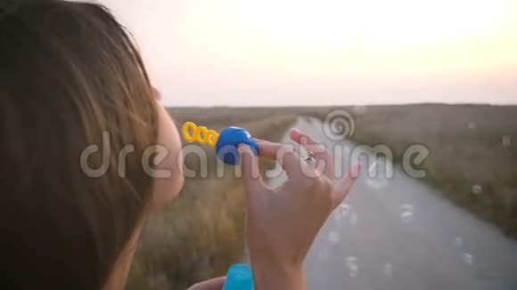 穿着鲜艳衣服的女孩在风中吹着肥皂泡晚上在马路的背景下微笑视频的预览图
