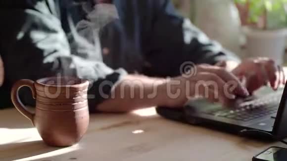 一个男人用笔记本电脑键盘上网喝热茶双手合拢视频的预览图