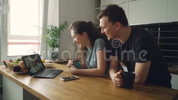 年轻快乐的白种人夫妇坐在笔记本电脑前的桌子上和他们快乐的积极晒黑的朋友一起飞翔视频的预览图