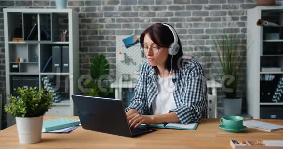 戴耳机的年轻女士在办公室里用手提电脑听音乐视频的预览图