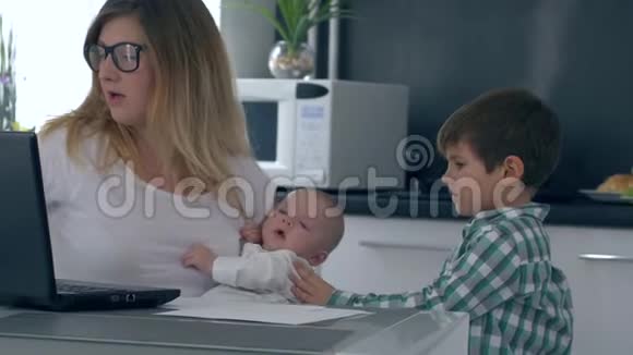 紧张的精神崩溃妈妈抱着孩子骂儿子干扰在家工作视频的预览图