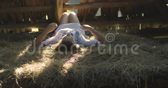 年轻女子在阳光下微笑晒在干草上木制棚子4K视频的预览图