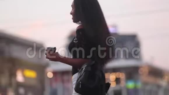 晚上带着一杯咖啡的年轻女子在城市街道上散步和微笑视频的预览图
