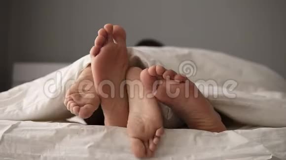 一对年轻美丽可爱的夫妇躺在床上他们的脚在毯子下而早上在床上醒来视频的预览图