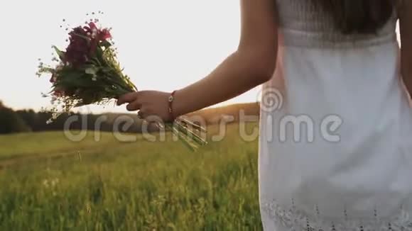夏天的晚上女人带着一束野花在田野里散步日落时分漫步在草地上视频的预览图