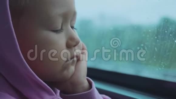 坐公共汽车时戴兜帽的悲伤的孩子望着潮湿的窗户视频的预览图