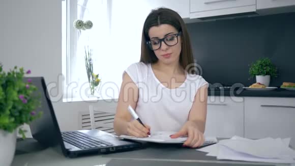 戴眼镜的商业妈妈坐在厨房的笔记本上做笔记然后高兴地抱着儿子视频的预览图