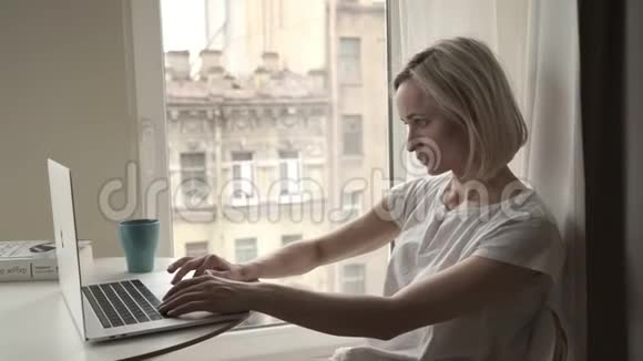 坐在靠窗的年轻女子在家里用笔记本电脑视频的预览图