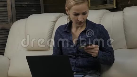 漂亮的女人坐在家里的沙发上用笔记本电脑和银行信用卡在线购物4K视频的预览图
