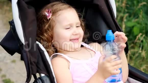 小女孩躺在婴儿车里喝着瓶子里的水夏天口渴视频的预览图