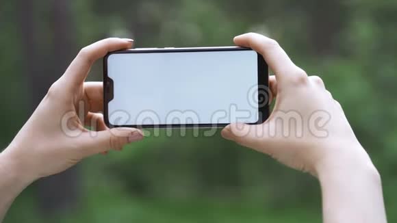 一个女孩在模糊的自然背景下持有智能手机概念移动互联网本质上的智能手机视频的预览图