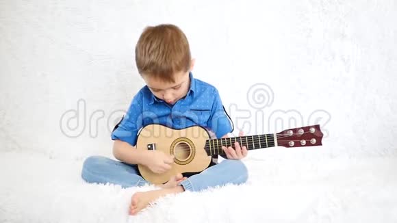 一个快乐的孩子坐在白色的沙发上为孩子们弹吉他视频的预览图