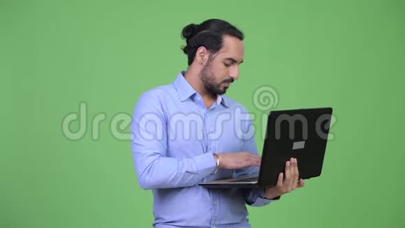 年轻的留着胡子的印度商人一边用笔记本电脑一边思考视频的预览图
