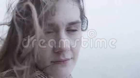 美丽的年轻女子站在户外雾天看着相机愁眉苦脸的女人的头发随风飘扬视频的预览图