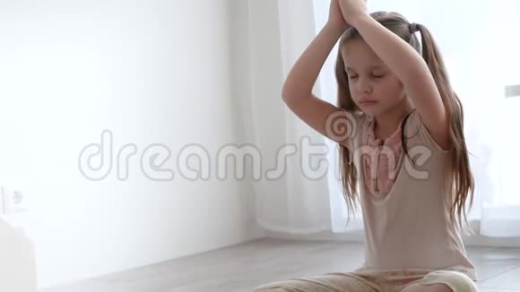 小可爱的女孩坐在瑜伽莲花的姿势在窗户附近冥想视频的预览图