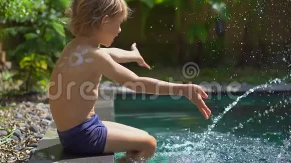 一个小男孩肩膀上有一个防晒霜吸引的太阳在游泳池里泼水太阳保护视频的预览图