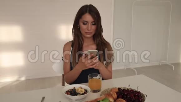 漂亮的女人带着手机吃早餐视频的预览图