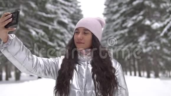 年轻女孩站在冬天的森林里用智能手机自拍视频的预览图