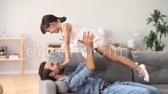 快乐的父亲躺在沙发上孩子女儿玩得很开心视频的预览图