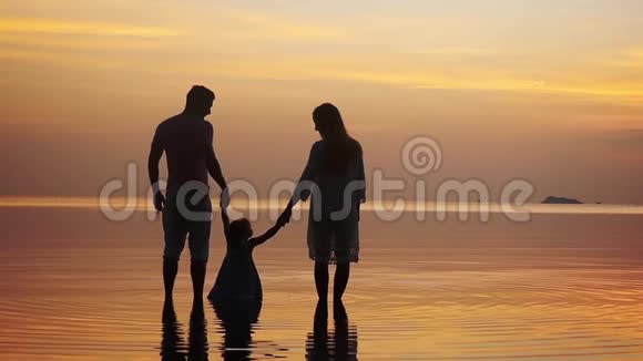 幸福的年轻一家人牵着手在令人惊叹的金色日落中沿着海岸散步家庭假日慢慢慢慢视频的预览图