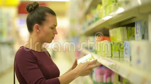 年轻女性从超市货架上挑选湿巾一个有白种人外表的女孩在超市购物高清高清视频的预览图