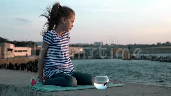 悲伤的女孩坐在海岸与他的鱼一个圆形水族馆户外夏天概念视频的预览图