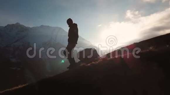 在美丽的日落中一个人在山的边缘行走的史诗般的照片的鸟瞰剪影视频的预览图