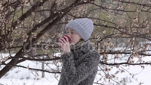 女孩正在一棵花树旁喝咖啡湿雪视频的预览图