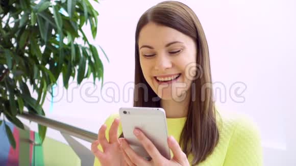 年轻漂亮的女人站在购物中心慢吞吞地笑着使用智能手机聊天视频的预览图