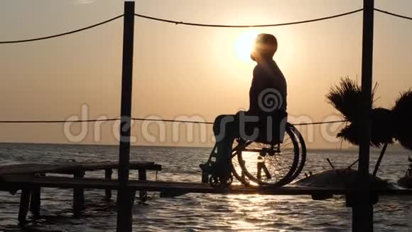 浪漫的约会女性和男性残疾人坐轮椅在码头附近的海面与夏季日落视频的预览图