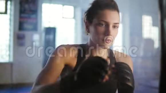 近距离观看白种人女拳击手在健身房用手套与烟雾击中拳击袋坚强视频的预览图