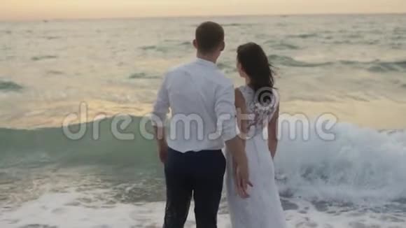 重新浪漫的景色美丽的新婚夫妇轻轻地牵着手在夕阳下享受大海视频的预览图