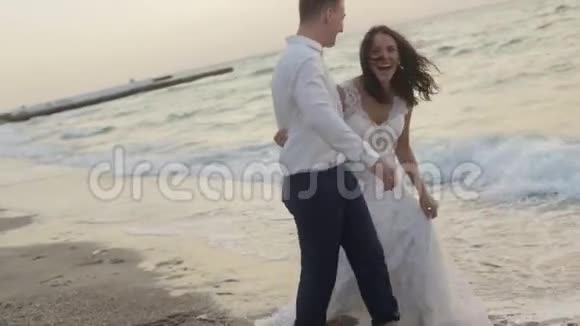 美丽的新娘和英俊的新郎在日落时在海滩上玩得很开心他们拥抱奔跑温柔视频的预览图