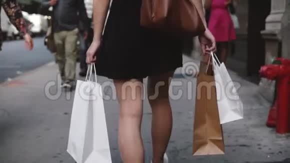 在买了很多新衣服后年轻的当地女孩带着购物袋沿着城市街道散步慢动作视频的预览图