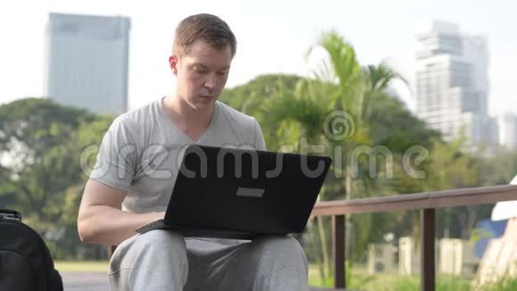 年轻的帅哥在公园的木桥上用笔记本电脑视频的预览图