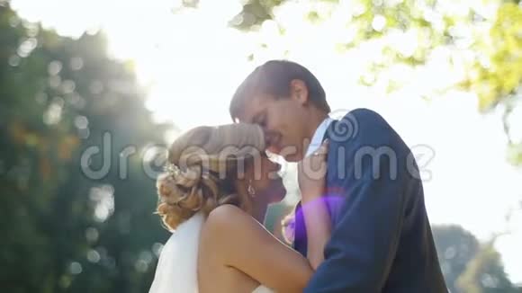 漂亮的年轻夫妇在阳光下温柔地拥抱和亲吻新婚夫妇英俊的新郎亲吻他的爱人视频的预览图