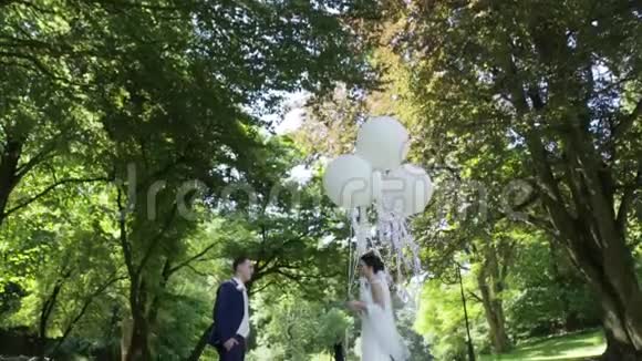 幸福的新婚夫妇在春天公园里温柔地拥抱和亲吻新娘拿着白色气球视频的预览图