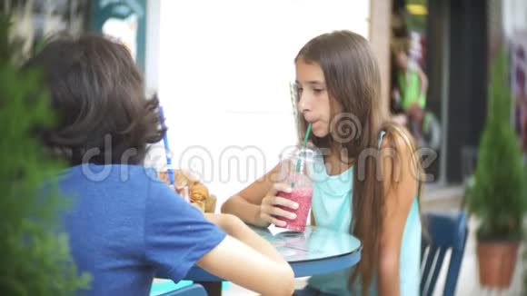 十几岁的男孩和女孩坐在街头咖啡馆的桌子旁喝鸡尾酒4k慢动作视频的预览图