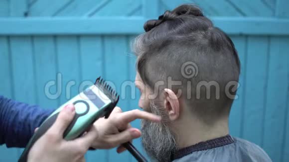 漂亮的女理发师给留着胡子的漂亮男人剪头发电动剃须刀和梳子视频的预览图