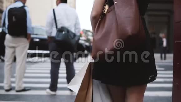 回头看匿名的年轻女子带着一个时尚的袋子等待穿过街道拿着购物袋慢动作视频的预览图