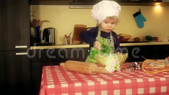 可爱的小厨师女孩带厨师帽和围裙混合面粉准备沙漠视频的预览图
