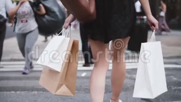 后景成功的年轻女子穿着短黑色连衣裙带着购物袋穿过街道慢动作视频的预览图