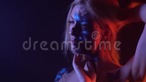 一个金发女郎脸上画着蝴蝶的身体站在蓝色和红色的灯光下视频的预览图