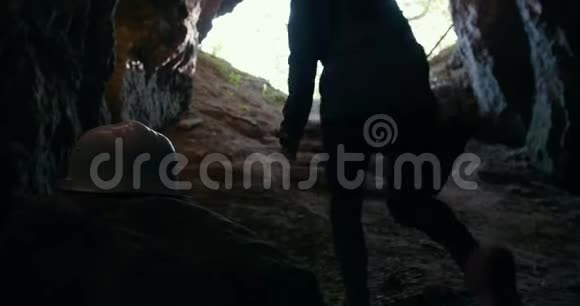 戴着头盔的年轻徒步旅行者从黑暗的洞穴里爬上来视频的预览图