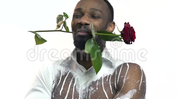特写镜头穿白色简易衬衫的黑帅哥用红玫瑰和笑保持牙齿视频的预览图