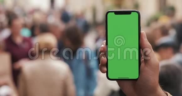 特写一个男人手握着并使用绿色屏幕移动小工具街道上有一个垂直的绿色屏幕视频的预览图