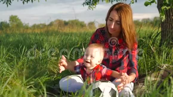 妈妈和她的小儿子正坐在公园的草地上玩足球幸福的家庭视频的预览图
