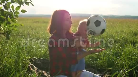 妈妈和她的小儿子正坐在公园的草地上玩足球幸福的家庭视频的预览图
